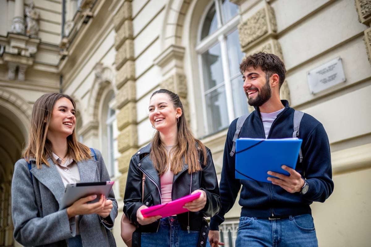 Three students holding books and chatting with laughter between classes