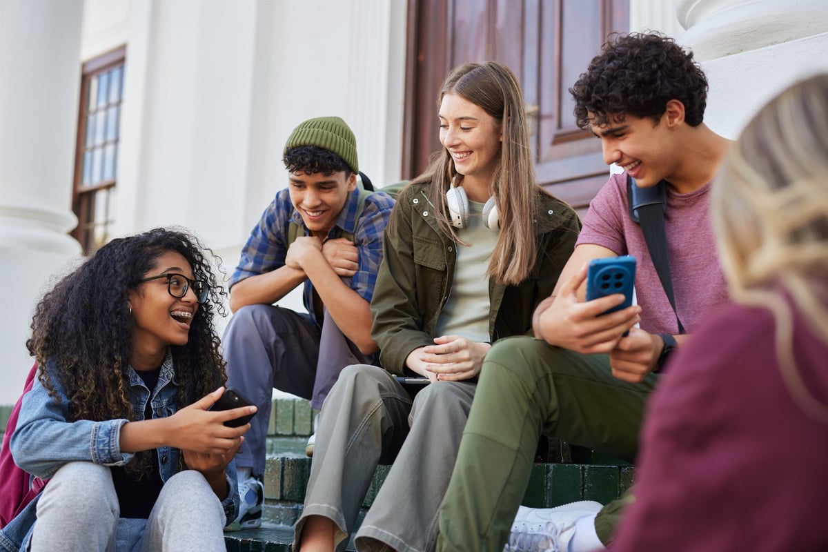 Multicultural students sitting together on campus steps, smiling and having fun