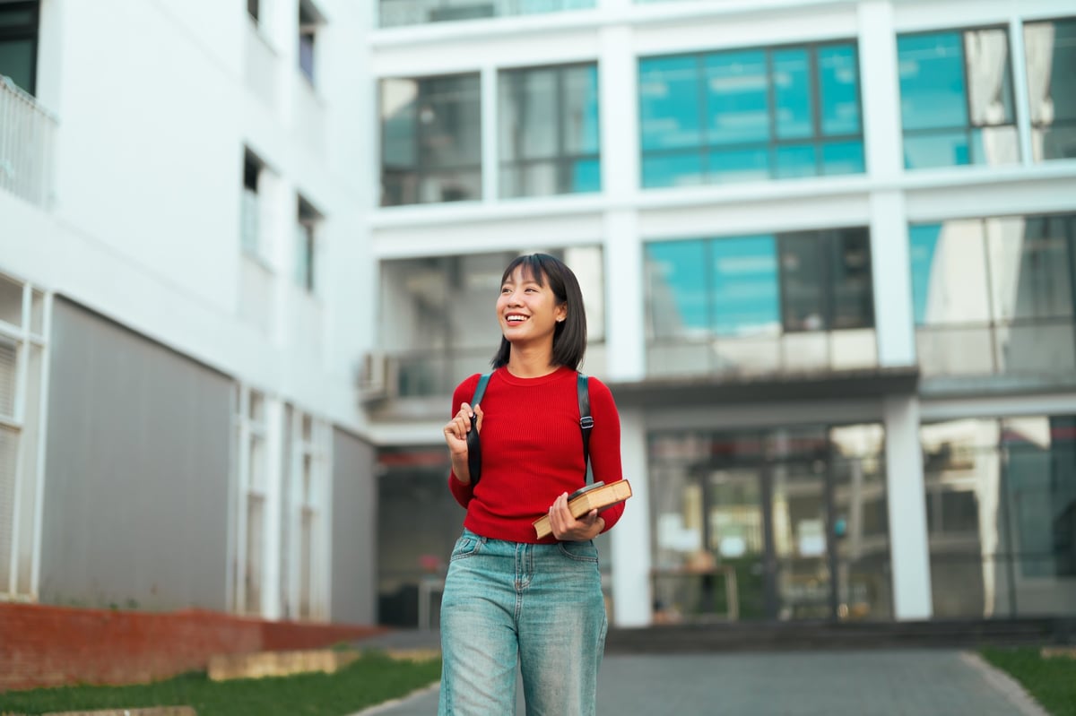 A happy student walking on a UK university campus carrying books
