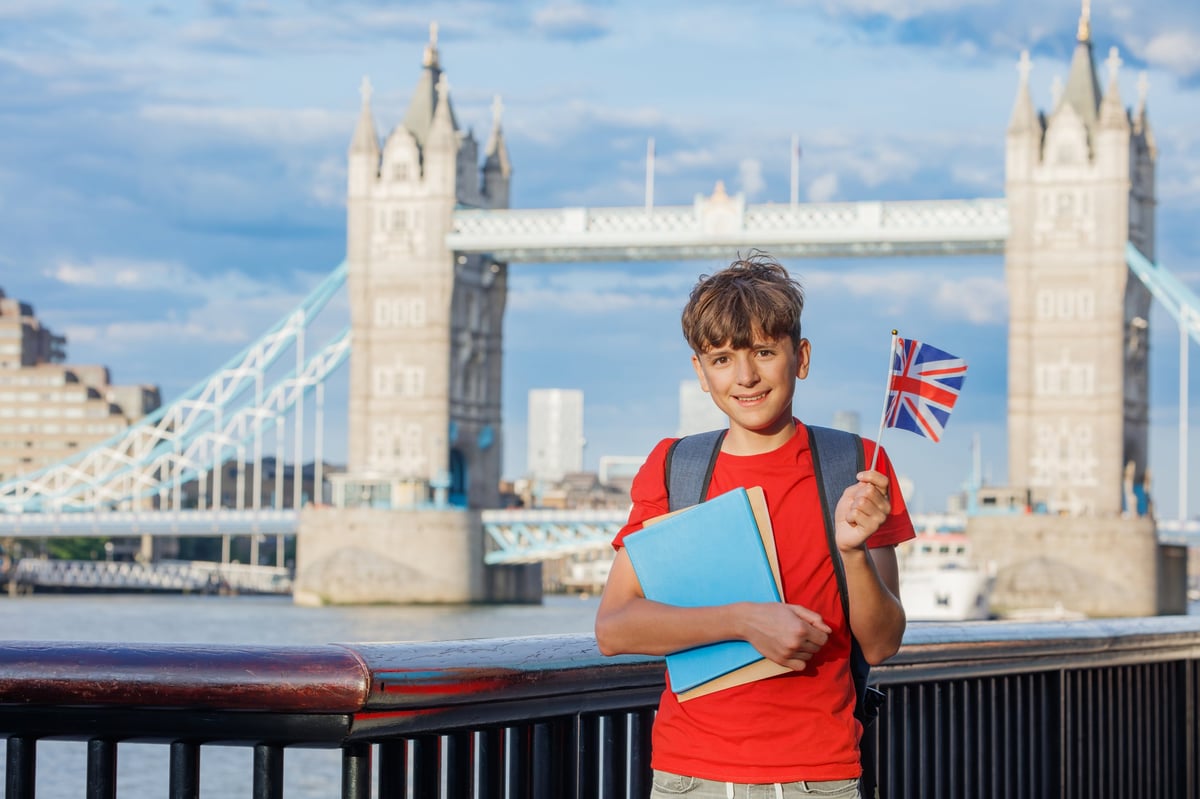 A young student holding books by the River Thames with Tower Bridge behind