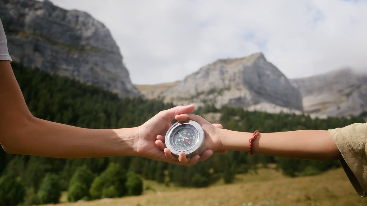 A hand guiding a child's hand with a compass, representing supported discovery