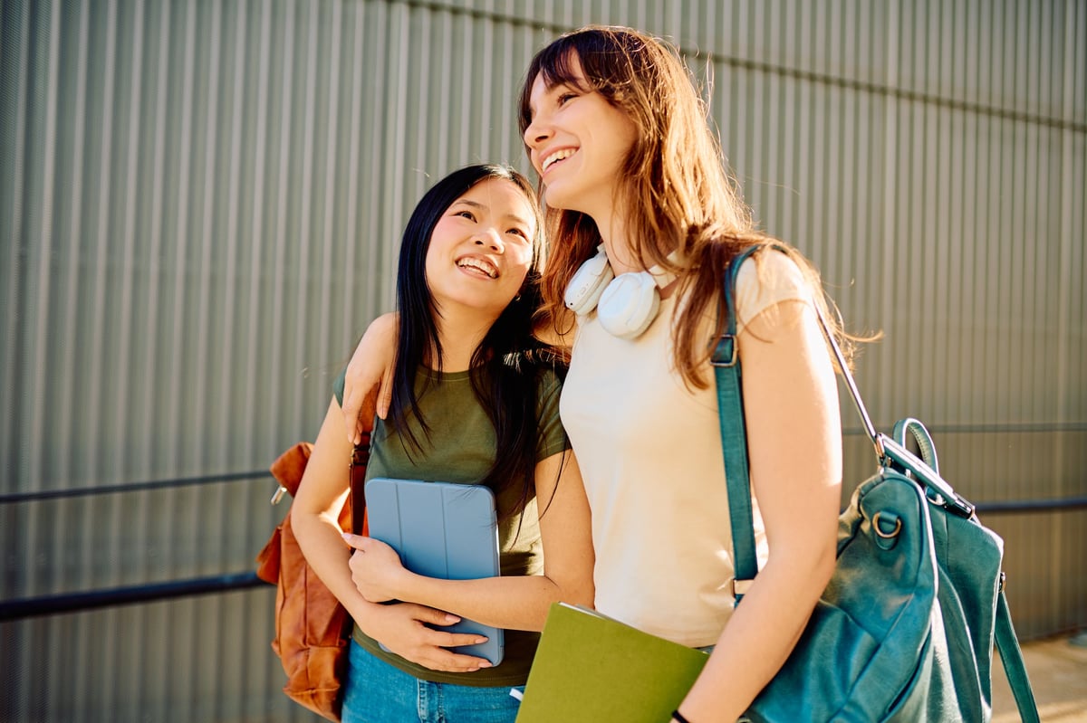Two cheerful young students walking together through friendship on a university campus
