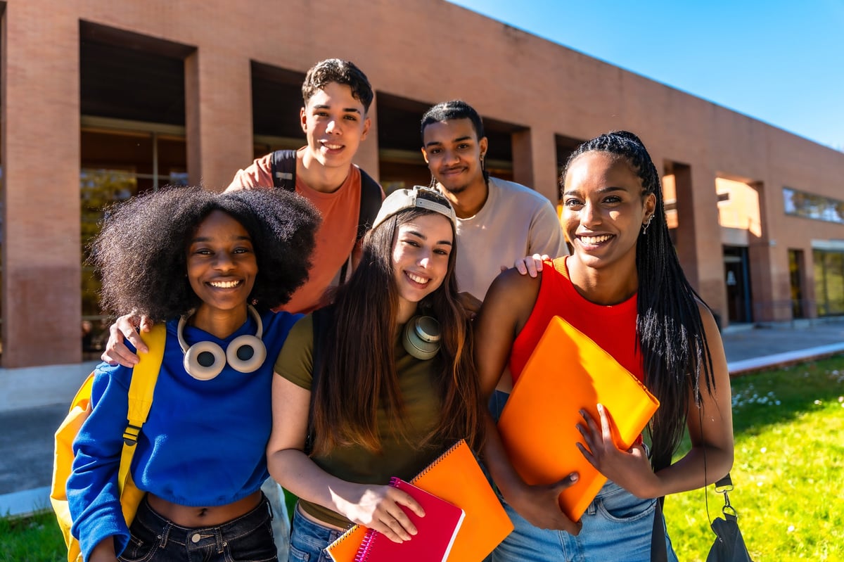 A group of students standing proudly together on campus, holding books