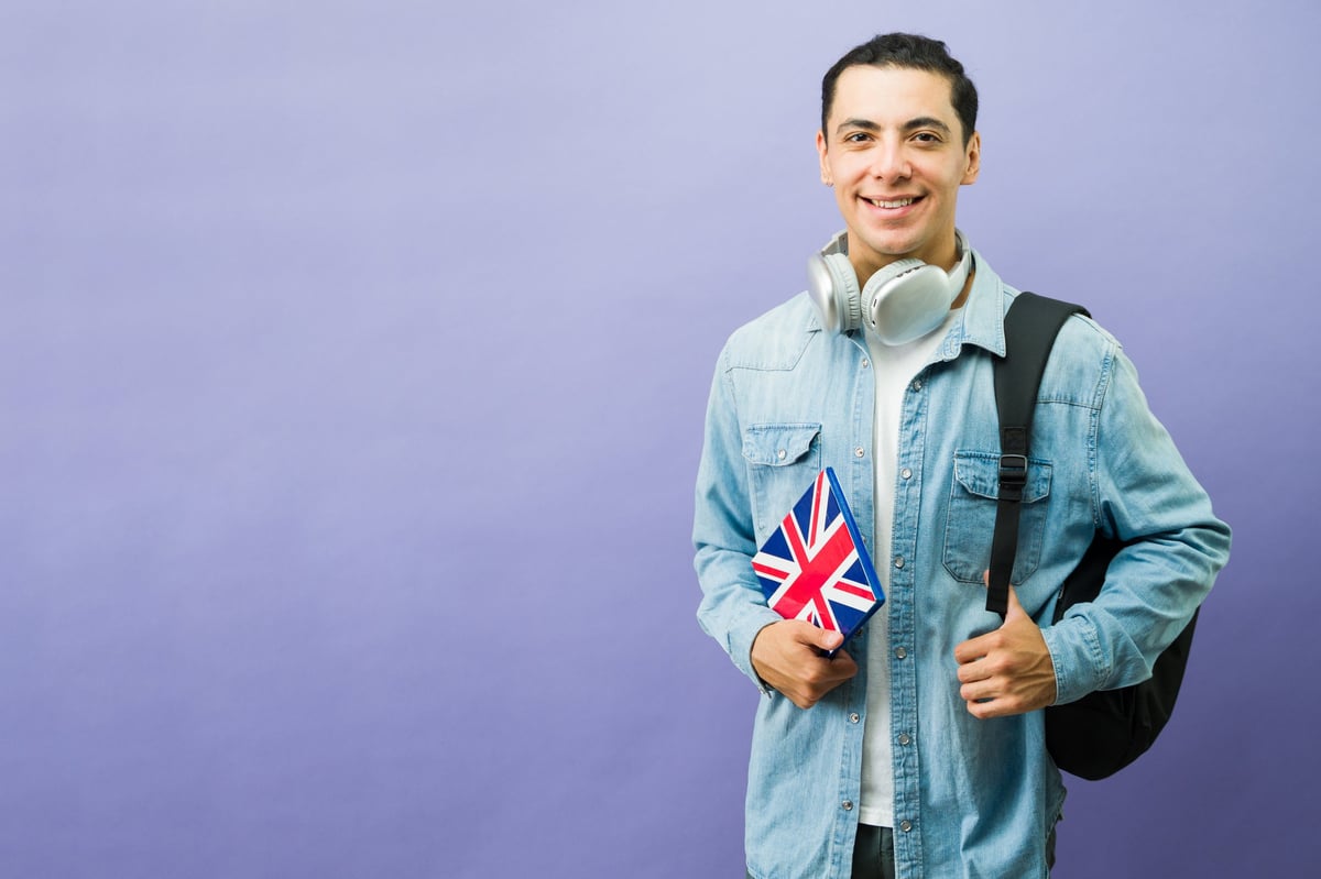 Happy student holding an English language book and wearing headphones